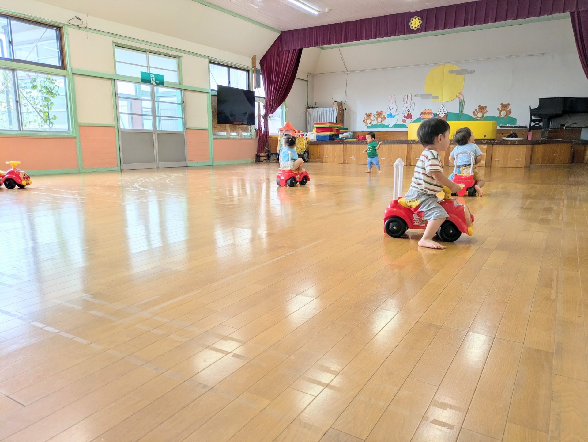 広いホールでこどもたちが車のおもちゃに乗って遊んでいます